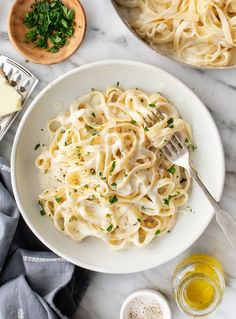 a white bowl filled with pasta and parsley on top of a marble countertop