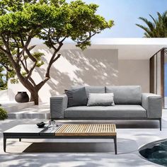 an outdoor living area with couches, coffee table and pool in the background on a sunny day