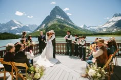 a bride and groom are kissing on the deck at their wedding in front of mountains