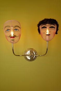 two masks are on the wall, one has a candle in its mouth and the other has a nose