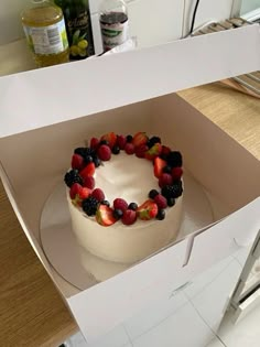 a white cake with berries and strawberries in a box on top of a counter