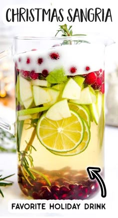 a pitcher filled with liquid and fruit on top of a white table next to christmas decorations