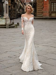 a woman in a white wedding dress standing on a cobblestone area with buildings behind her