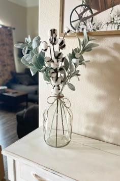 a vase filled with flowers sitting on top of a white dresser next to a painting