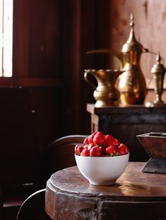 a bowl of strawberries sitting on top of a wooden table