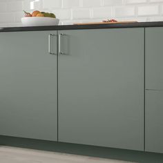 a kitchen with green cupboards and white tile backsplash, black countertop