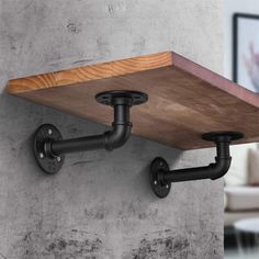 a wooden shelf mounted to the side of a wall with black pipe fittings on it