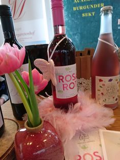 some wine bottles and pink tulips in a vase on a table with other wines