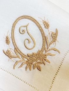 an embroidered monogram on the side of a white shirt with gold thread and flowers