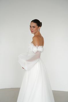 a woman in a white wedding dress standing with her arms on her hips and looking off to the side