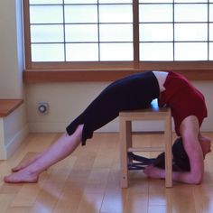 a person doing a handstand on top of a wooden table in front of a window