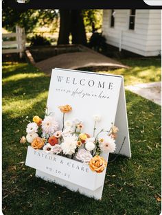 a welcome sign sitting on top of a lush green field next to a white house