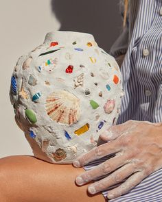 a woman with her arm wrapped around a rock covered in sea glass and seashells