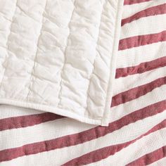 an unmade bed with red and white striped sheets on it's side, next to a pillow