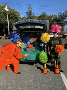 two people dressed as clowns standing in front of a car with its trunk open