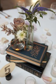 there is a vase with flowers on top of three books at the center of this table