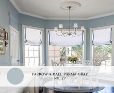 a dining room with blue walls and white furniture in the center, surrounded by windows that have roman shades on them