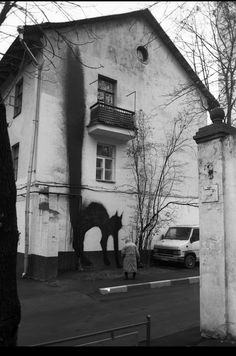 an old photo of a horse painted on the side of a building with a woman walking past it