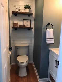 a white toilet sitting inside of a bathroom next to a wooden shelf filled with towels