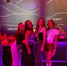 four girls are posing for the camera in front of a bar with neon lights on it