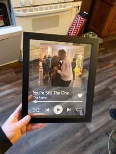 a person holding up a framed photo with the words you're still the one on it