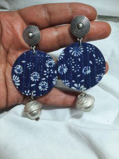 a pair of earrings with blue and white flowers on them is being held in someone's hand