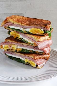 two sandwiches stacked on top of each other with ham and egg in between them, sitting on a white plate