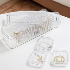 three clear containers with gold jewelry on a white table