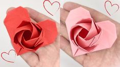 two origami roses in the palm of someone's hand with hearts drawn on them