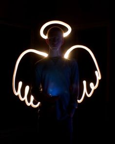 a man standing in the dark with an angel light painting on his face and arms