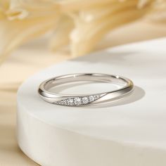 a white gold wedding band with three diamonds on the side, sitting next to a flower