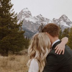 a bride and groom kissing in front of the mountains with their arms around each other