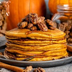 a stack of pancakes with walnuts and syrup being drizzled on top