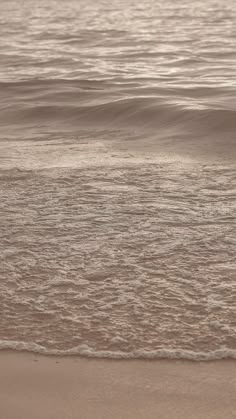 a person walking on the beach with their surfboard in hand and water behind them