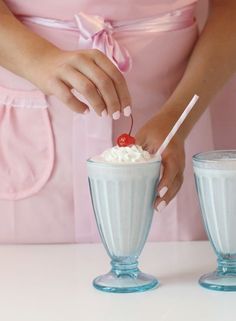 a woman in a pink dress is holding a strawberries and milkshake with whipped cream