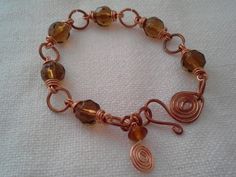 a copper wire bracelet with brown glass beads and spirals on the clasp is sitting on a white cloth