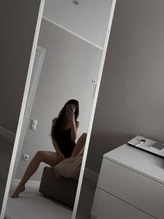 a woman sitting on top of a couch talking on a cell phone next to a dresser