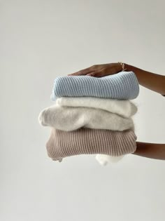 a person holding three different colored sweaters on their hands, one is white and the other is blue