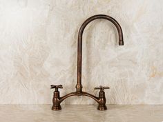 a faucet with two handles on a marble countertop in front of a wall