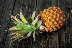 a pineapple sitting on top of a wooden table next to another piece of fruit