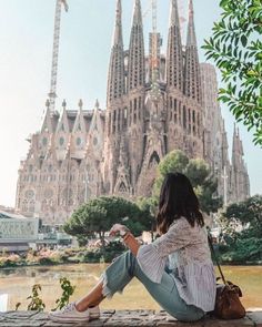 a woman sitting on the ground in front of a large building with towers and spires