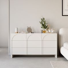 a living room with white furniture and plants on the top of the cabinet, next to a couch