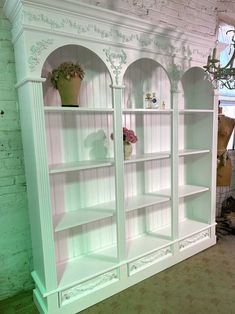 a white bookcase with flowers and vases on it