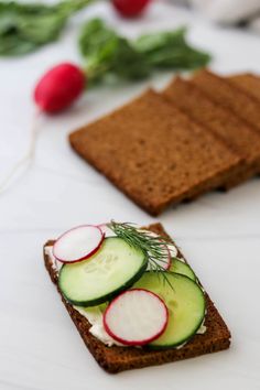 two slices of bread with cucumber and radishes on them, next to other food items