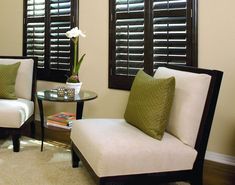 a living room with two chairs and a table in front of windows covered in blinds