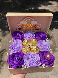 a person holding a box with purple flowers and chocolates in it's center