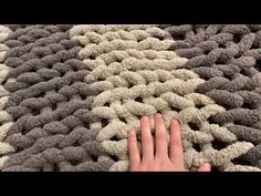 someone's hand is touching the top of a crocheted rug with grey and white colors