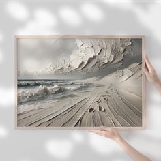 a person holding up a painting with white sand and water in the ocean behind it