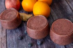 two glasses filled with chocolate smoothie next to oranges and apples