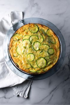 a pie with zucchini and cheese is on a plate next to a napkin